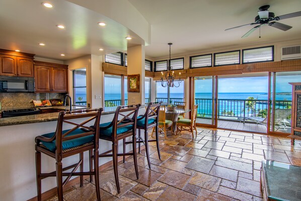 A spacious kitchen with a large island, wooden bar stools, and a view of the ocean through large sliding glass doors.