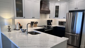 Eine moderne Küche mit weißen Schränken, einem Edelstahlkühlschrank, einem eingebauten Backofen und einer Marmorarbeitsplatte.