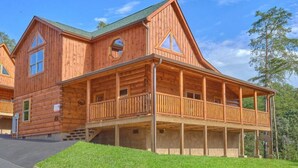 A wooden log cabin with a balcony, a covered porch, and a steeply pitched roof.