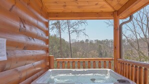 A wooden cabin with a hot tub on a balcony overlooking a forest.