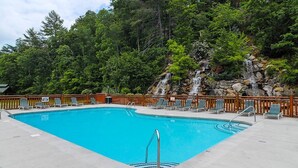 A rectangular pool with a wooden deck and lounge chairs, surrounded by a wooden fence and lush greenery.