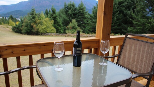 A glass table with two wine glasses and a bottle on a wooden deck with a mountain view. - Mt Defiance Cabin with Columbia River View (Stevenson)