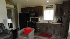 A compact living space with a gray armchair, a black refrigerator, a microwave, and dark wooden cabinets. - Mt Defiance Cabin with Columbia River View (Stevenson)