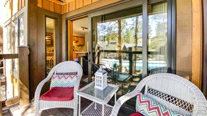 Une terrasse en bois avec des chaises en osier et une petite table, donnant sur une piscine et un espace cuisine.