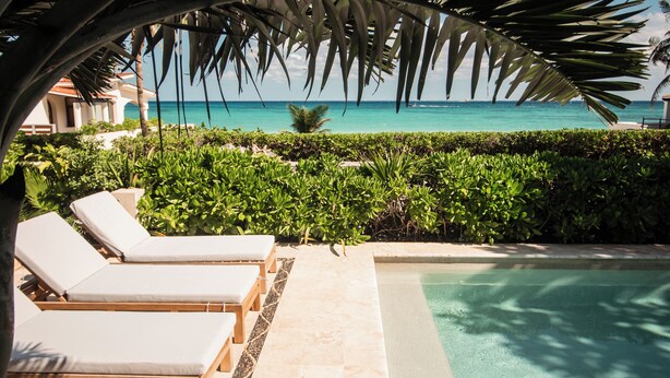 A pool area with lounge chairs, a clear view of the ocean, and lush greenery.