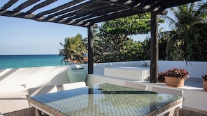 A glass-top table with cushioned chairs, a white wall, and a view of the ocean.