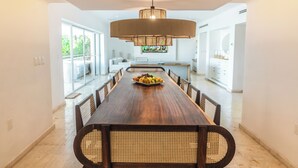 A modern dining area with a long wooden table, wicker chairs, and a central light fixture.