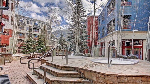 A public outdoor area with stone steps leading to a hot tub, surrounded by trees and buildings. - River Run Condo, 200 yards to gondola, Slope Views, Heated Garage, Free WiFi (Keystone)