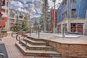 Un espace public extérieur doté d’un escalier en pierre menant à un jacuzzi, le tout entouré d’arbres et de bâtiments.