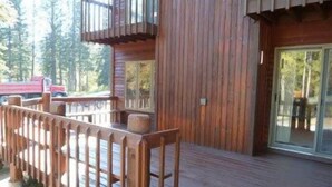 Une cabane en bois avec une terrasse, une porte en verre et un camion rouge en arrière-plan.