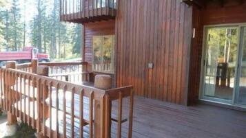 Une cabane en bois avec une terrasse, une porte en verre et un camion rouge en arrière-plan.
