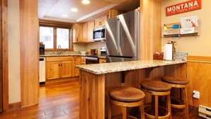 Une cuisine dotée de meubles en bois, d’un réfrigérateur en acier inoxydable, d’un comptoir en granit et d’un coin bar avec des tabourets.