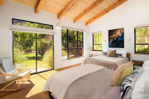 Quarto com janelas amplas, uma cama, uma cadeira e um quadro.