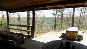 Una cabaña rústica con porche, chimenea de piedra y vistas al bosque circundante.
