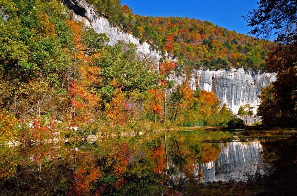 A serene lake with a cliff and autumn foliage.