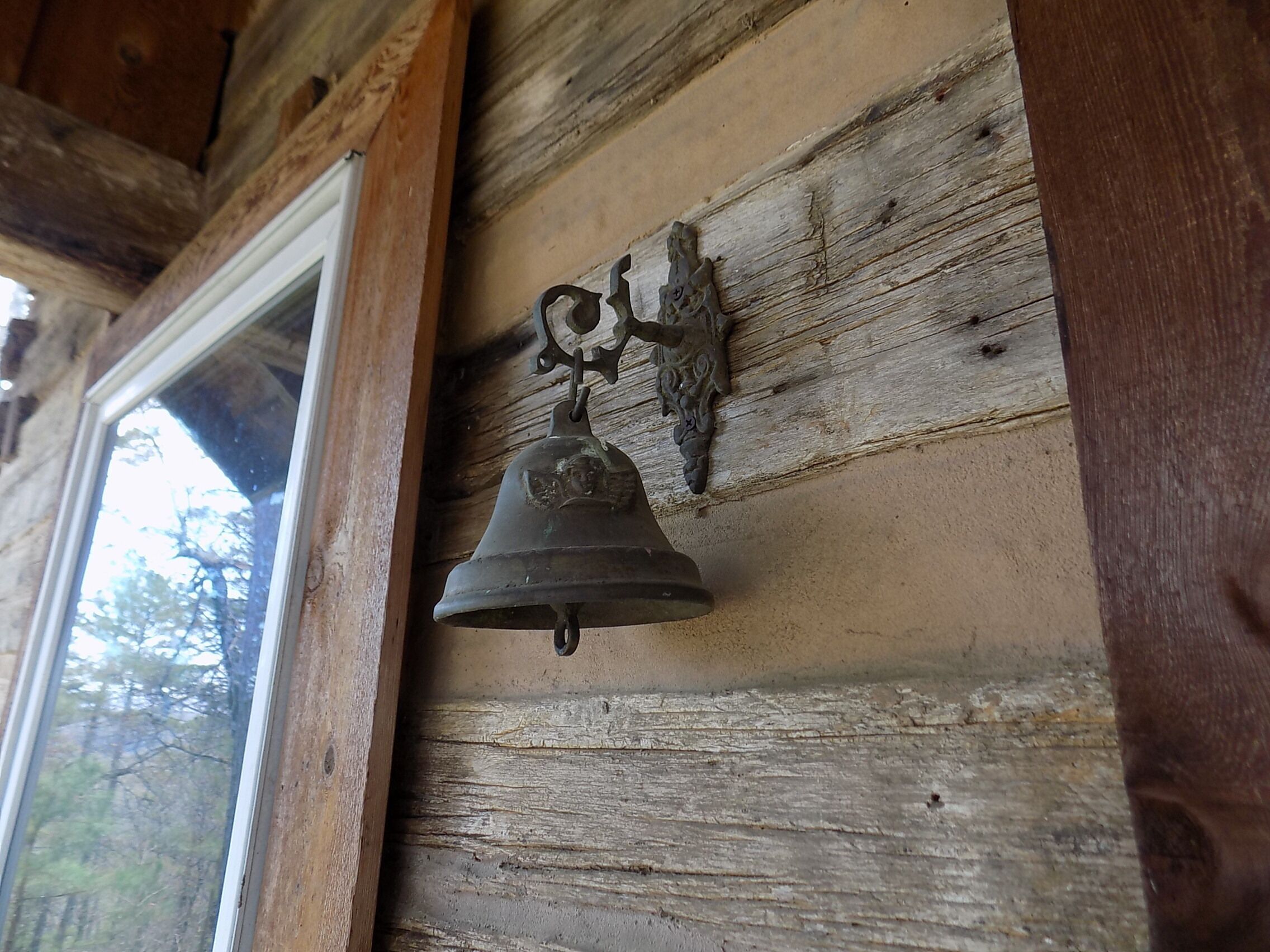 Un mur en bois rustique, sur lequel est fixée une vieille cloche en métal.