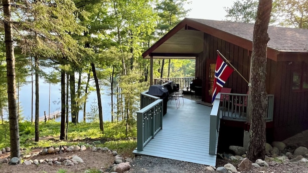 Una cabaña con terraza, una bandera y vistas al lago.