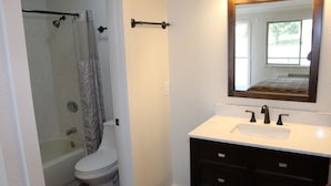 Une salle de bain équipée d’une baignoire, de toilettes, d’un meuble-lavabo avec des tiroirs et d’un miroir.
