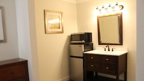 Une salle de bain compacte avec un lavabo blanc, un meuble-lavabo en bois foncé, un four à micro-ondes et un réfrigérateur.