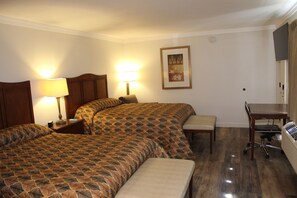 A hotel room with two beds, a desk, a chair, and a TV.
