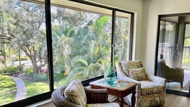 Una habitación con ventanas amplias, mobiliario de mimbre y una mesa de vidrio.