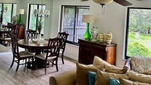 Un comedor con mesa y sillas, un ventilador de techo y vistas al exterior a través de amplios ventanales.