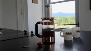 Una cocina con cafetera, dos tazas y ventana con vistas a zonas verdes y montañas.