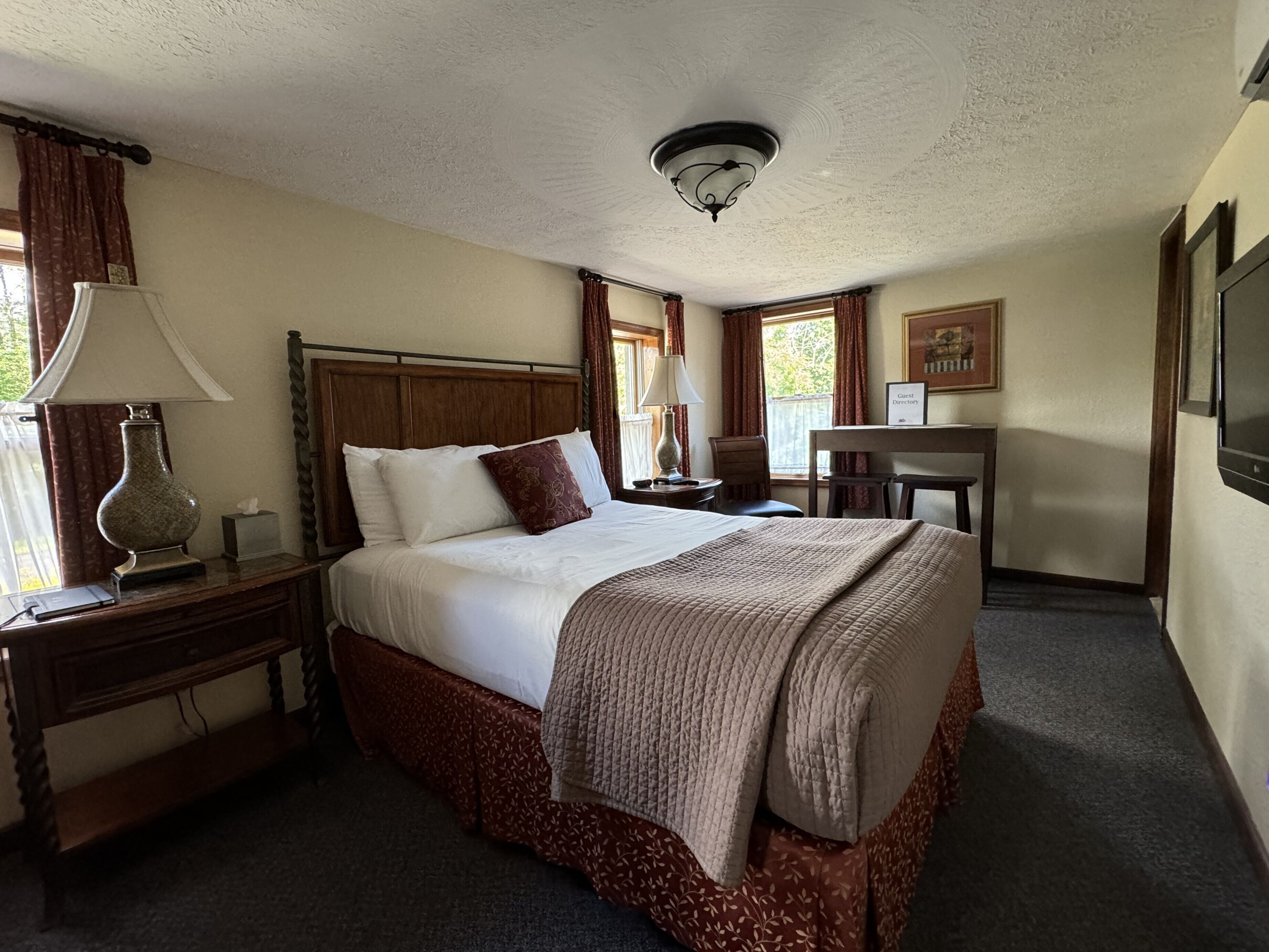 A hotel room with a large bed, a nightstand with a lamp, a desk, and a chair.