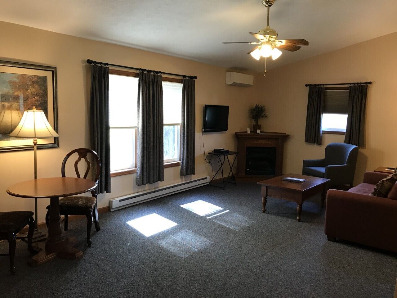 Una sala de estar con chimenea, ventilador de techo, televisor y un comedor con mesa y sillas.
