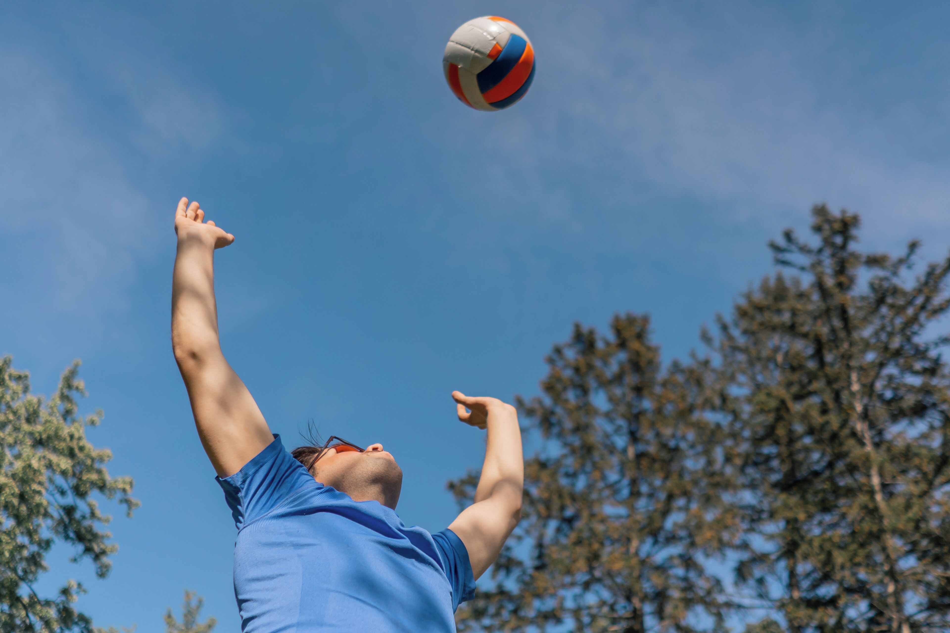 A person in a blue shirt reaching up to hit a volleyball.