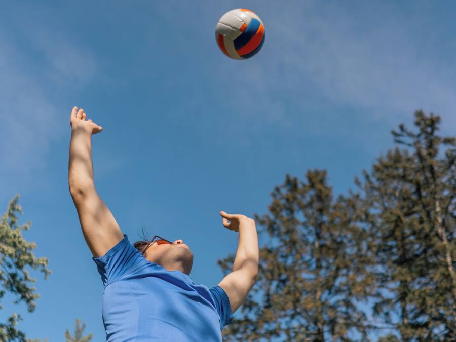 A person in a blue shirt reaching up to hit a volleyball.