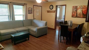 A living room with a gray sectional sofa, a coffee table, a dining table with chairs, a ceiling fan, and a painting on the wall.