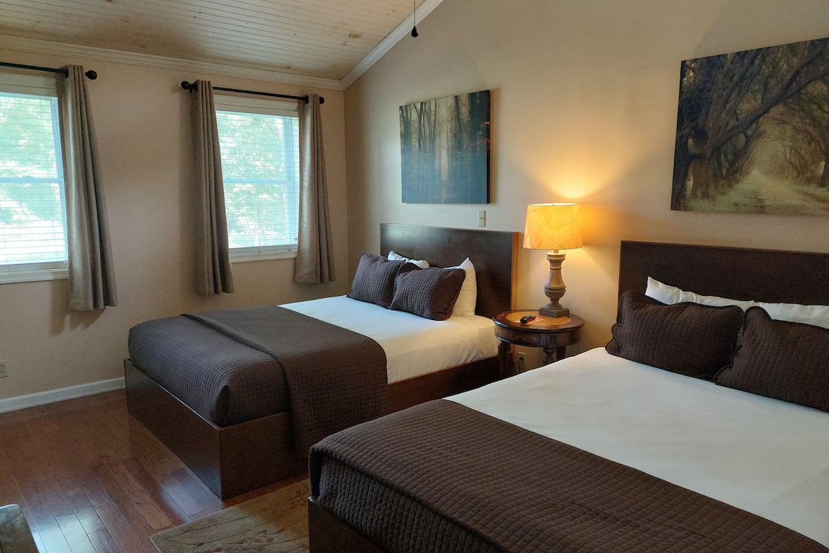 Habitación de hotel con dos camas, una mesita de noche con lámpara, un cuadro en la pared y una ventana con cortinas.
