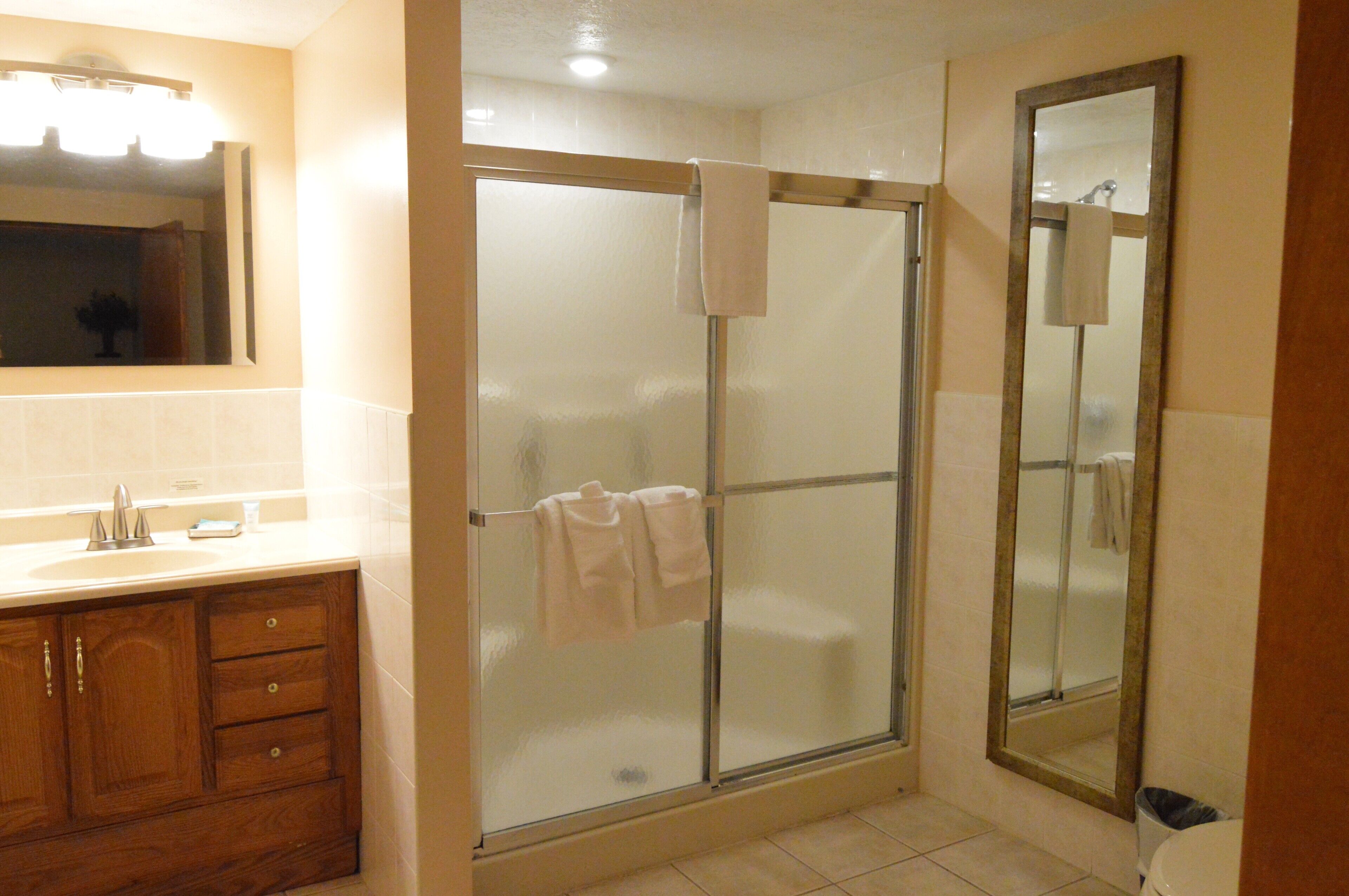 A bathroom with a glass-enclosed shower, a wooden vanity, and a large mirror.