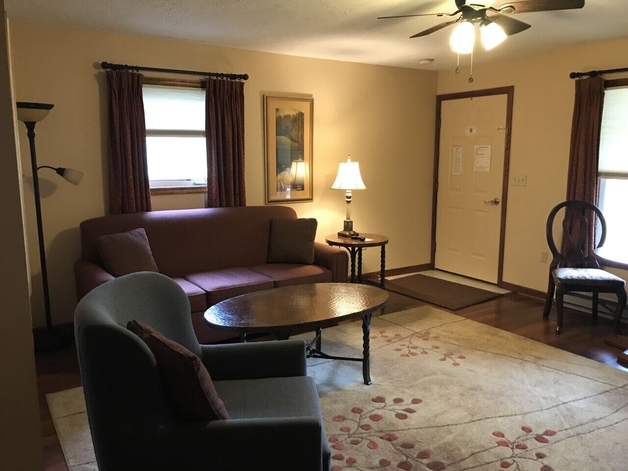 Ein Wohnzimmer mit einer Couch, Sesseln, einem Couchtisch, einer Lampe und einem Deckenventilator.