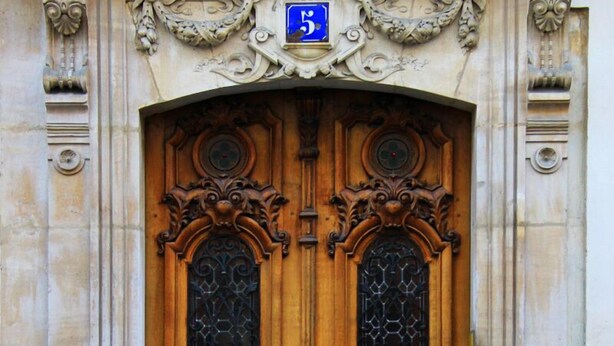 A double wooden door with intricate carvings and a blue sign above it.