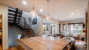 Un vaste espace dédié à la salle à manger, avec une grande table en bois, un escalier et un coin salon confortable agrémenté d’une cheminée.
