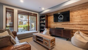 Un salon moderne comprenant un canapé, une table basse en bois, une bibliothèque, une cheminée et un téléviseur fixé à un mur en bois.