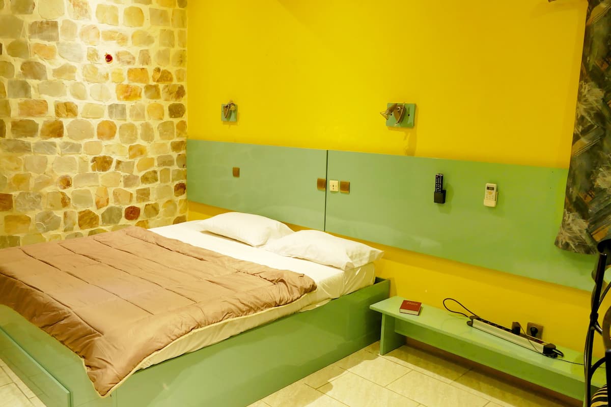 Une pièce avec un mur en pierre, un lit doté d’une tête de lit verte et une table de chevet sur laquelle se trouvent un livre et un téléphone.