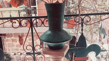 A balcony with a green vase holding red flowers, a metal railing, and a brick wall in the background.