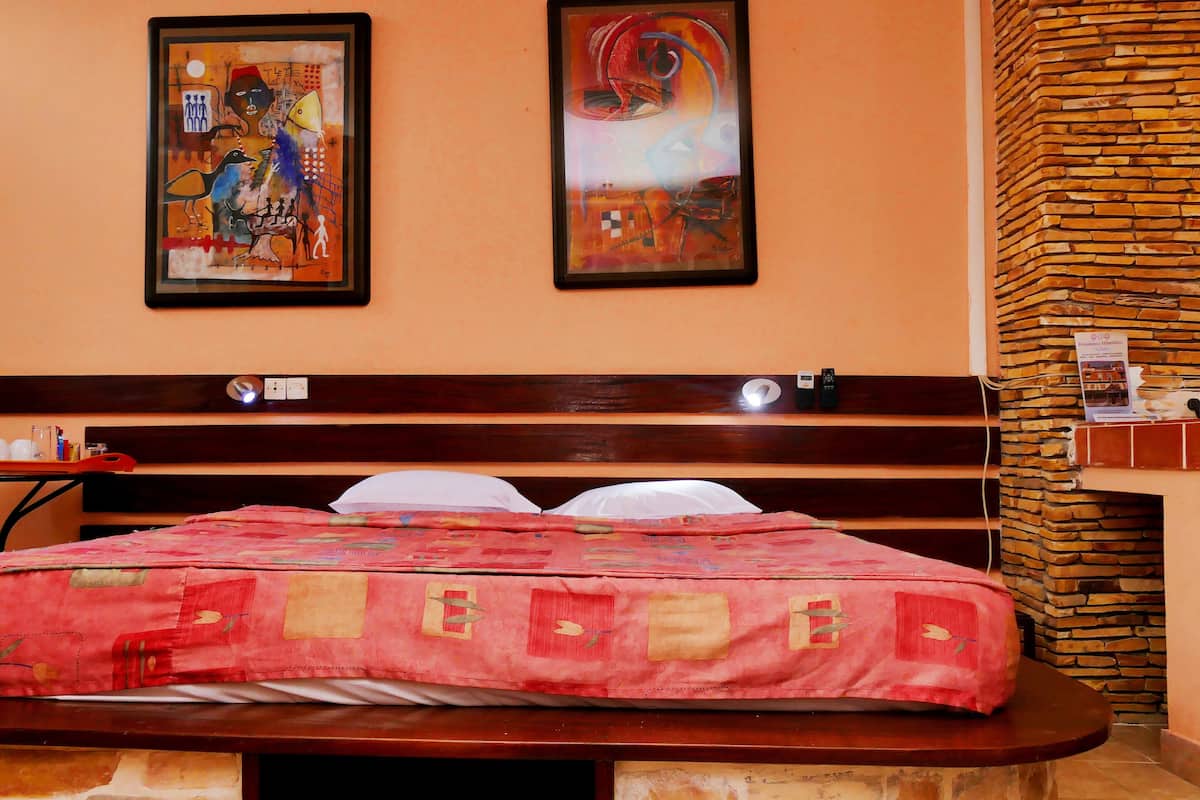 Une chambre d’hôtel avec un lit, une tête de lit en bois, deux œuvres d’art encadrées au mur, un mur décoratif en briques et une petite table sur laquelle se trouvent une tasse et des gobelets rouges.