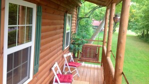 A wooden cabin with a porch, two white chairs with red cushions, and a hanging planter.