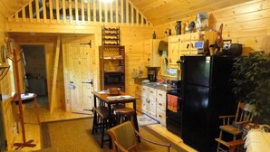 A cozy cabin interior with a dining area, kitchen, and a staircase leading to an upper level.