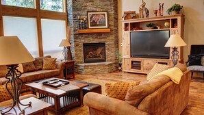 Een gezellige woonkamer met een stenen openhaard, leren banken, een flatscreen-televisie en houten meubels.