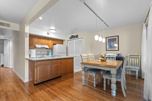 Una cocina con armarios de madera, un refrigerador blanco y una zona de comedor con mesa y sillas de madera.