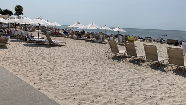 Una spiaggia con file di lettini e ombrelloni, cielo sereno e l'oceano sullo sfondo.