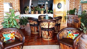 Un coin repas accueillant, avec des chaises en osier et une table centrale, entouré de plantes en pot et d’un mur en briques.