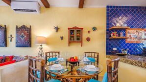 Un coin repas avec une table ronde dressée pour quatre personnes, entourée de chaises en osier avec des coussins bleus.