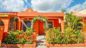 Un bâtiment à la façade d’un orange éclatant, agrémenté d’une arche décorative ornée de fleurs et entouré d’une végétation luxuriante.
