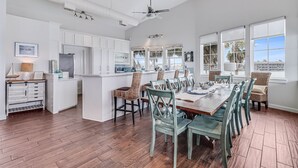 A spacious kitchen with white cabinetry, a central island, and a dining area with a large wooden table and matching chairs. - Sunsets | Private Pool & Hot Tub | Green Lights | Boat Lift | Icemaker (Rockport)